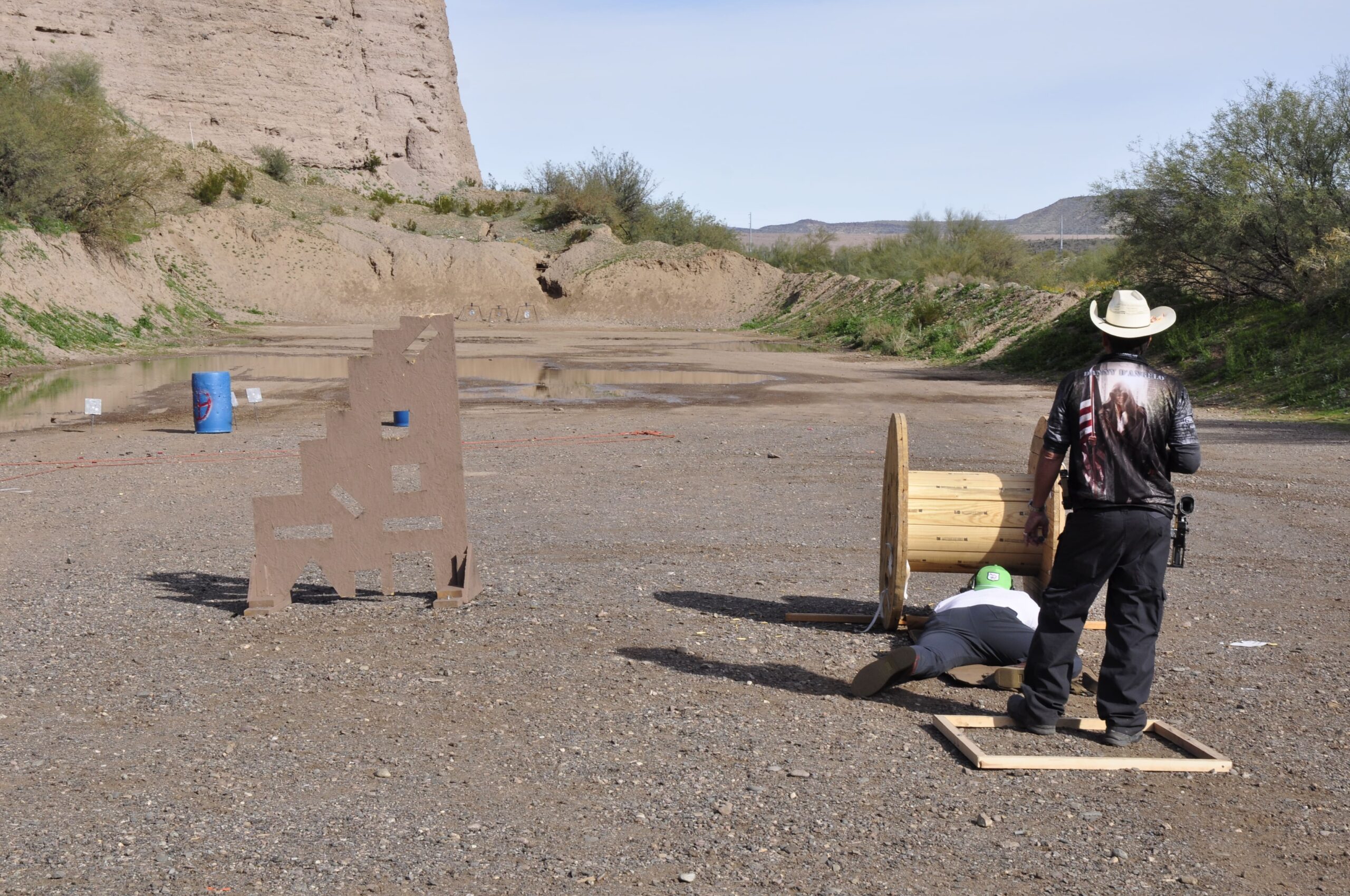 An operator utilizes barricades and landscape features for movement-based drills at Cowtown Range. The rugged terrain highlights the "Freedom to Train" essence of the facility.