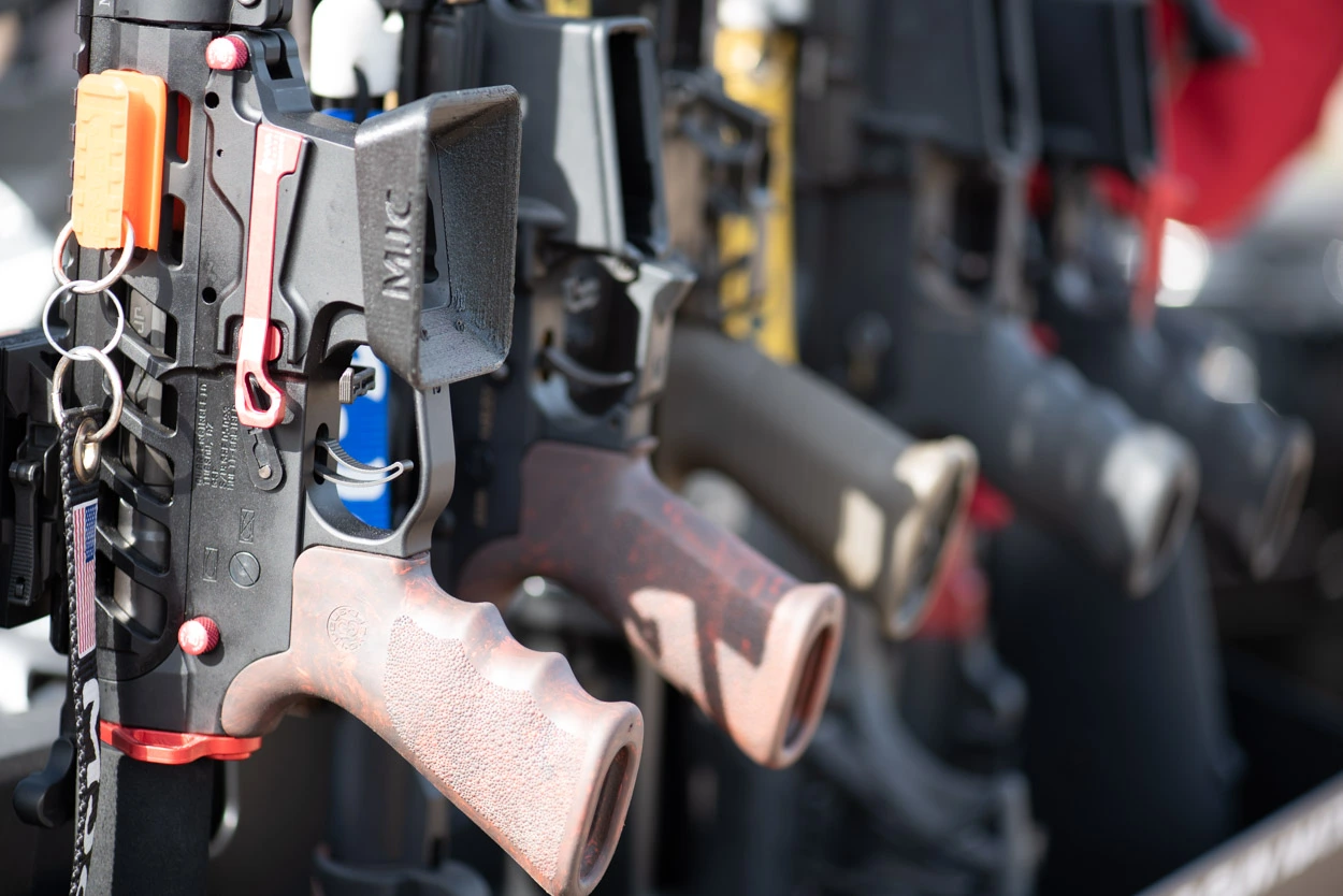 A close-up, shallow-focus shot of high-end rifle platforms lined up at Cowtown Range, featuring technical details like red accent pins, textured grips, and a branded American flag lanyard.