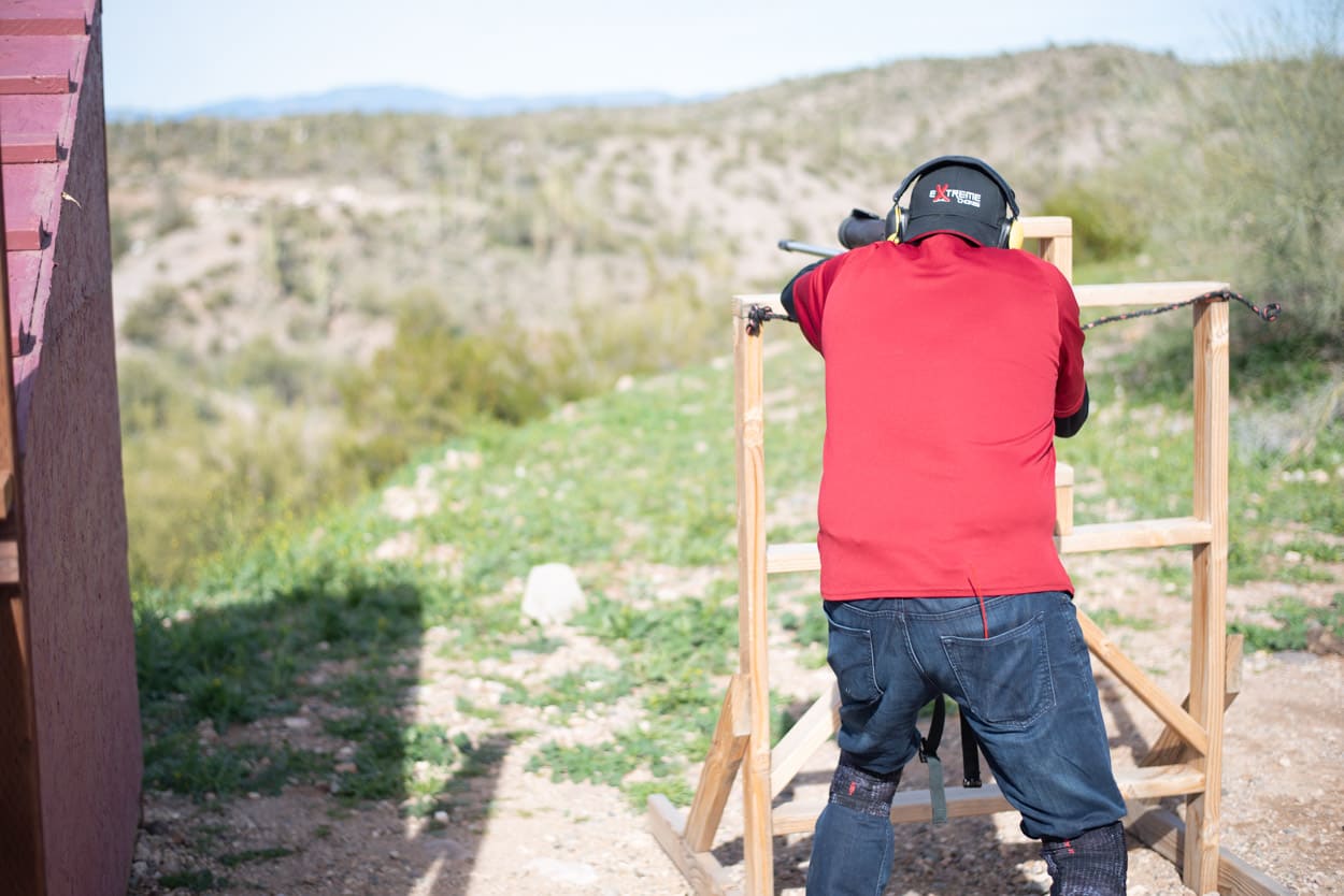 A serious practitioner engages a platform system from a wooden support structure, looking downrange at the expansive high-desert mirage.