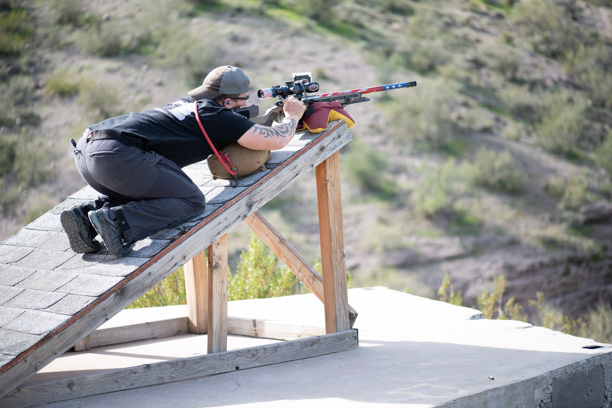 A shooter in a kneeling position practices unconventional positional shooting on a steep wooden ramp prop at Cowtown Range.