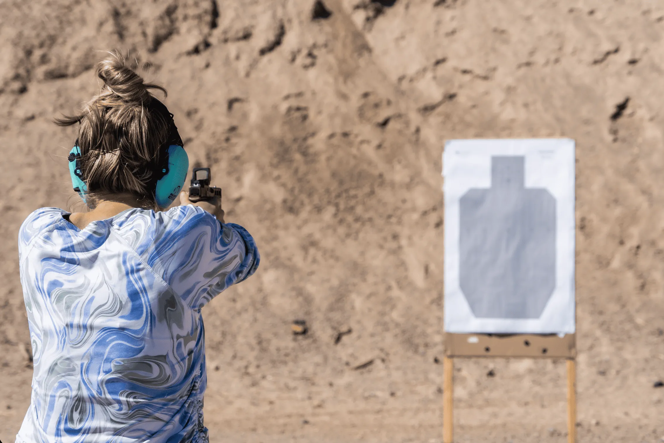 Shooter aiming a handgun at a paper silhouette target on an outdoor dirt range at Cowtown Range.