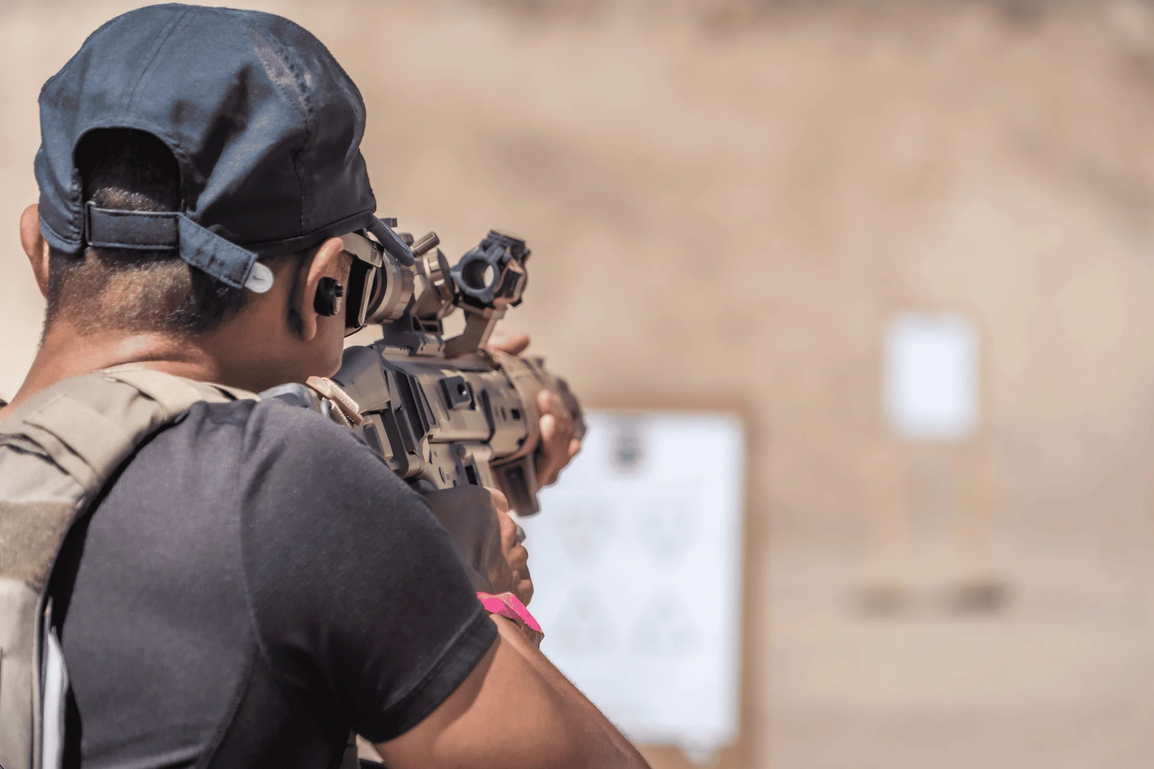 Over-the-shoulder close-up of a tactical shooter establishing a proper cheek weld and optic sight alignment with a carbine platform during a defensive training scenario.
