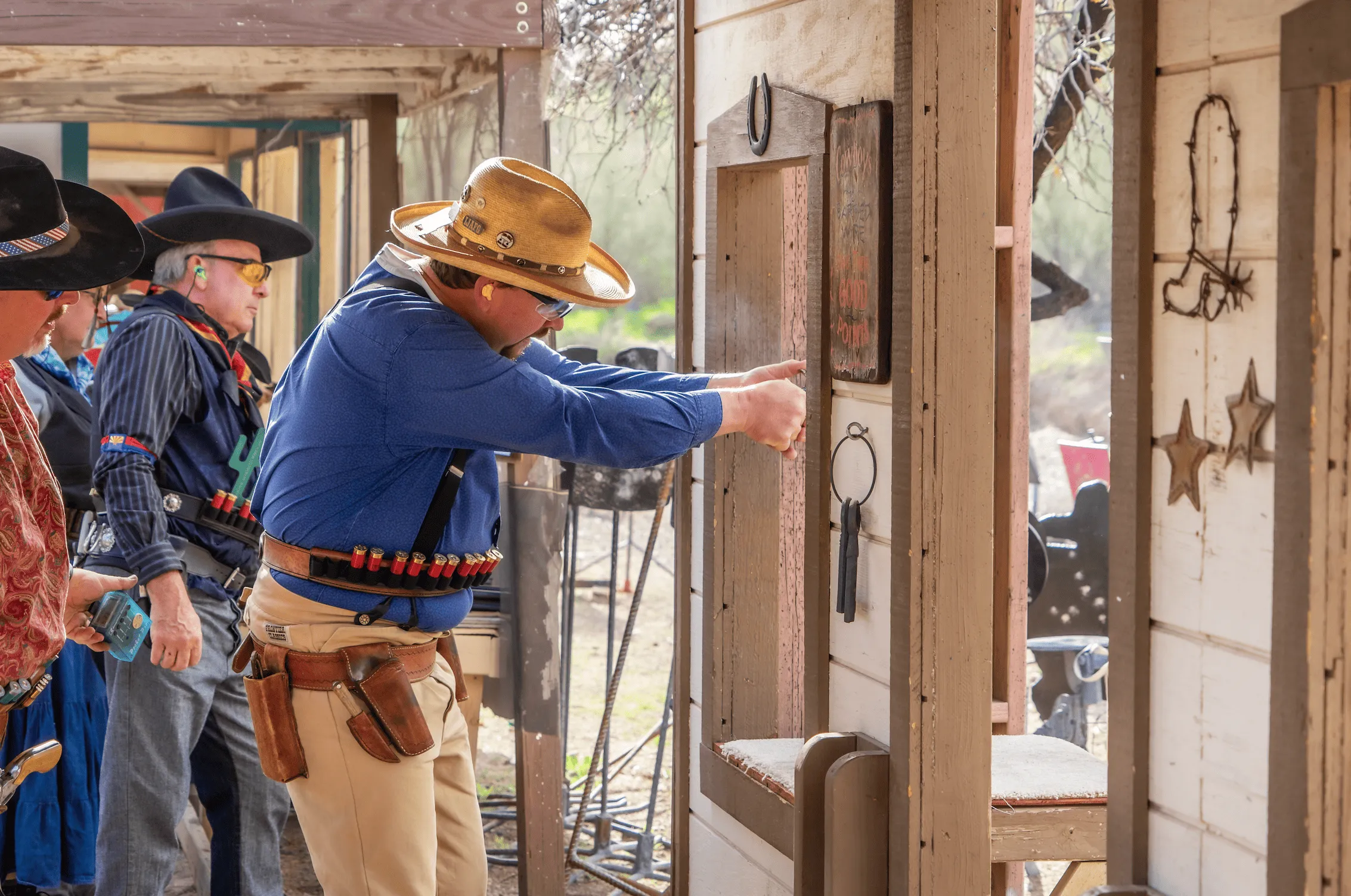 Shooter in cowboy hat and leather belt firing revolver through a western wooden stage window at Cowtown Range. (
