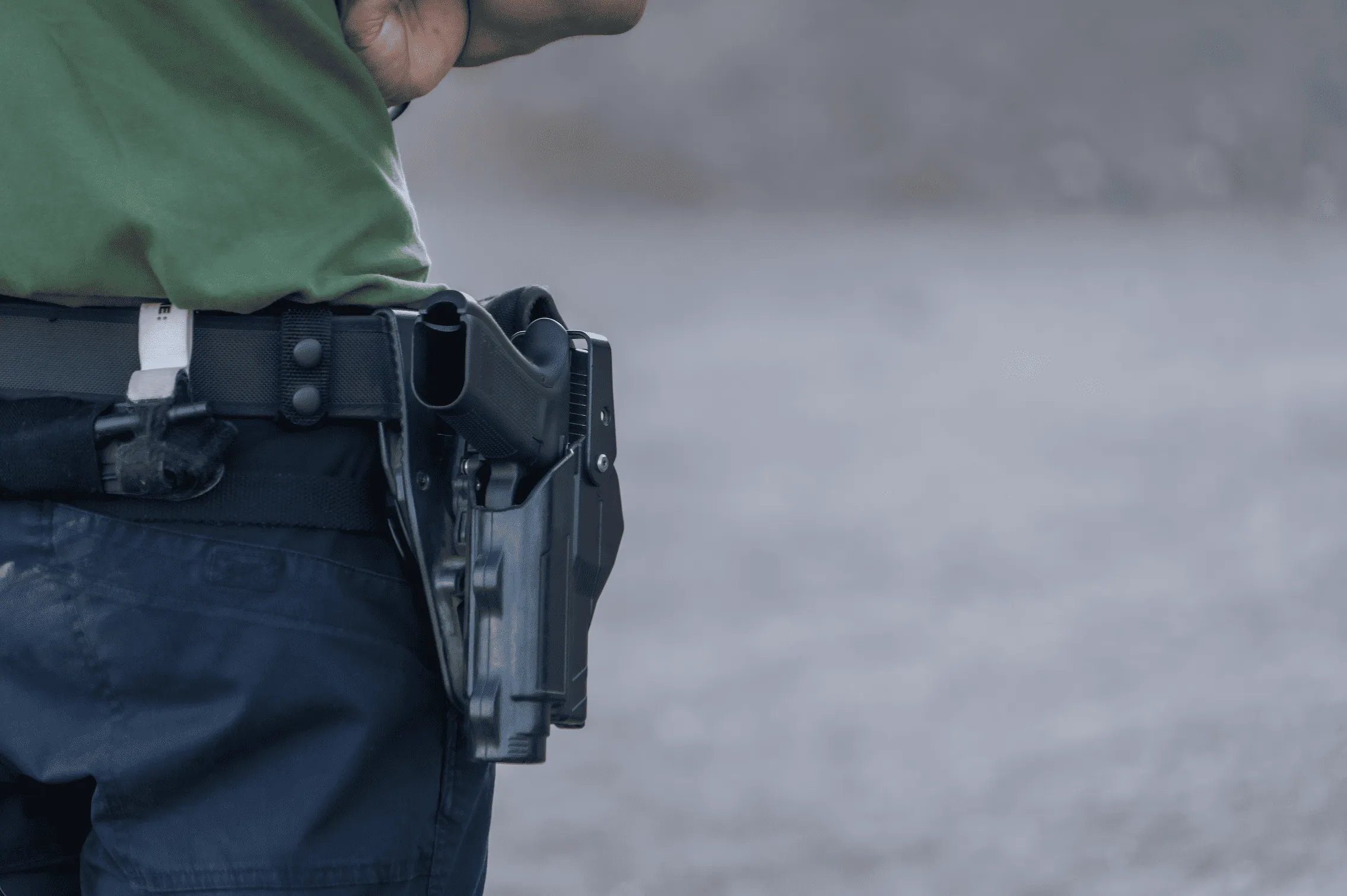 Close-up of a shooter wearing a handgun in a tactical belt holster at an outdoor shooting bay.