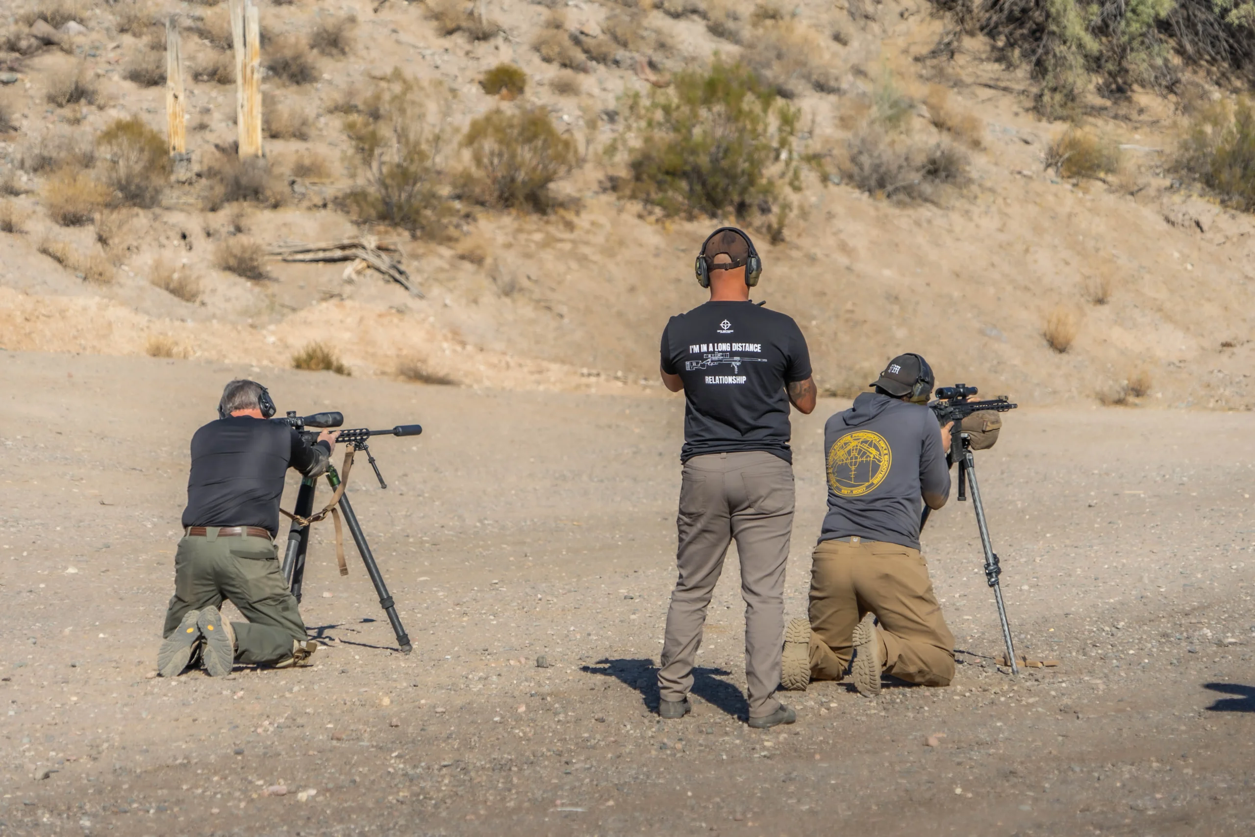 Shooters engage targets at distance using tripod-stabilized precision rifles on an elevated canyon platform.
