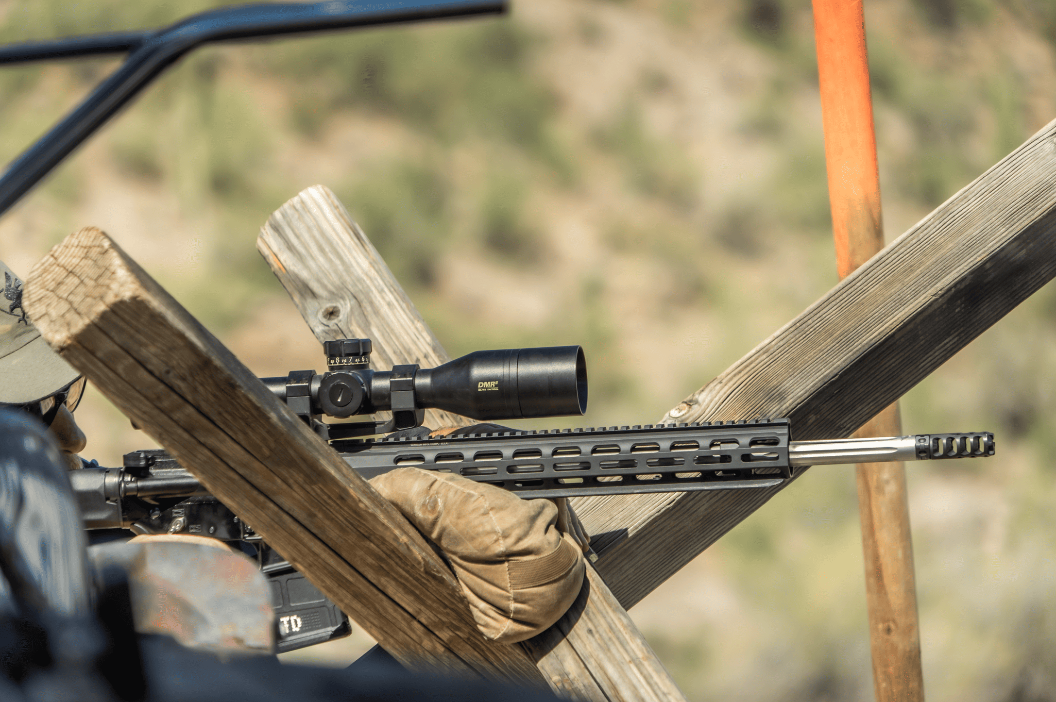 Close-up of a marksman stabilizing a scoped rifle system on a wooden barricade with a sandbag support during an outdoor precision training session at Cowtown Range.