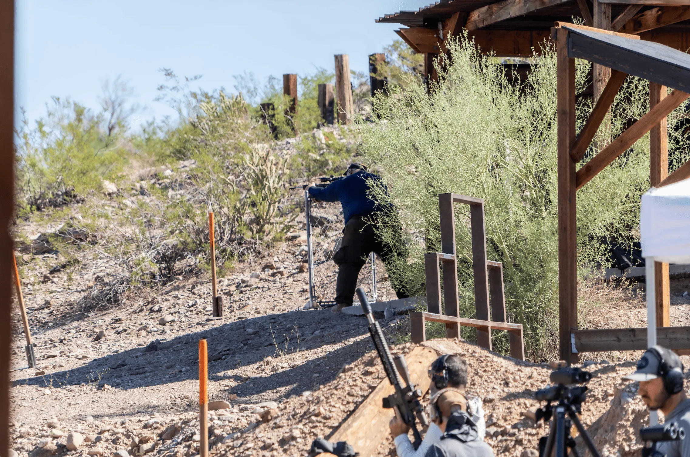 Precision rifle shooters conducting long-range training exercises from a barricade on an outdoor bay.