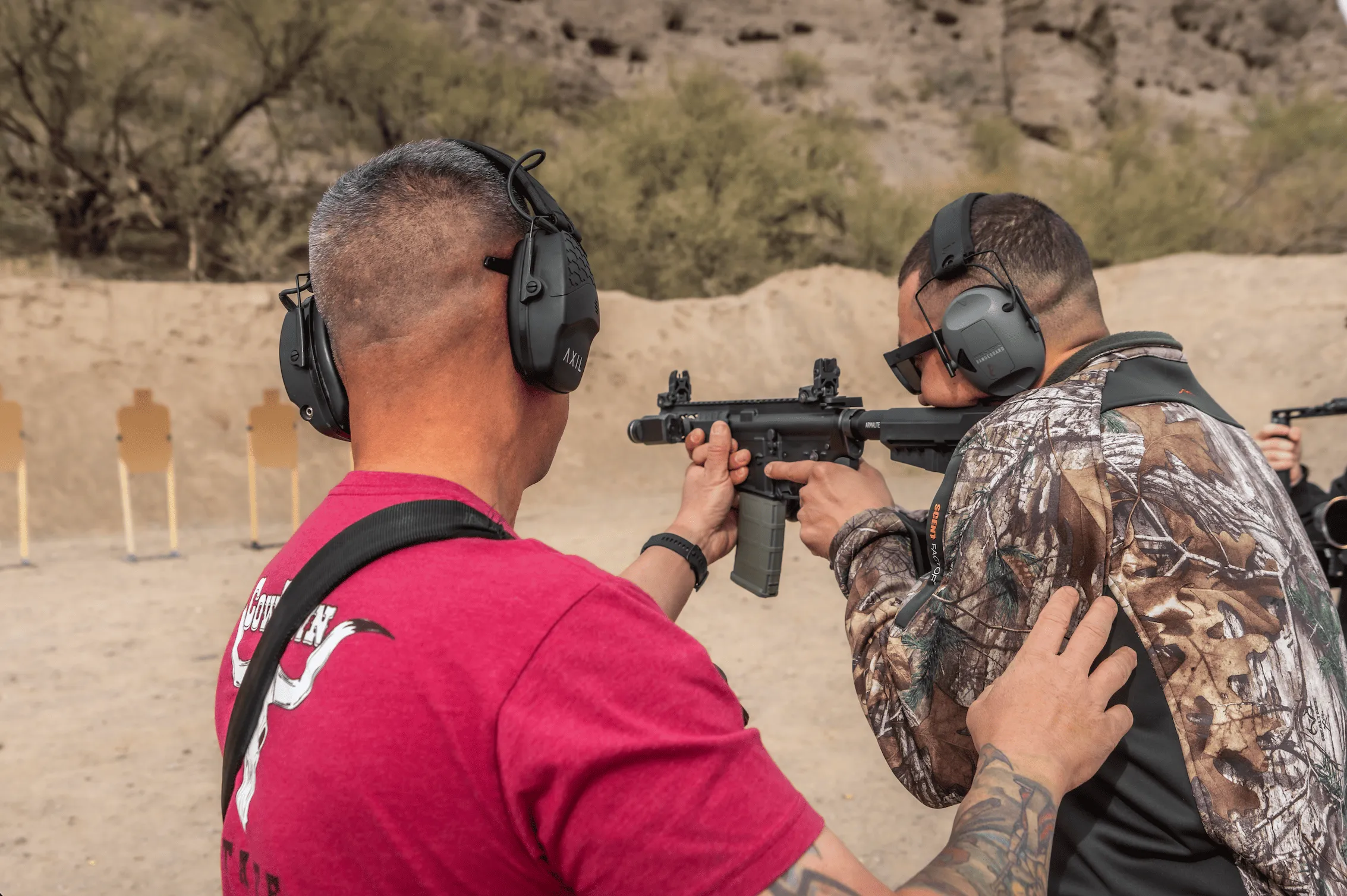 Former military instructor guides a shooter on platform mechanics and recoil control in an outdoor training bay.