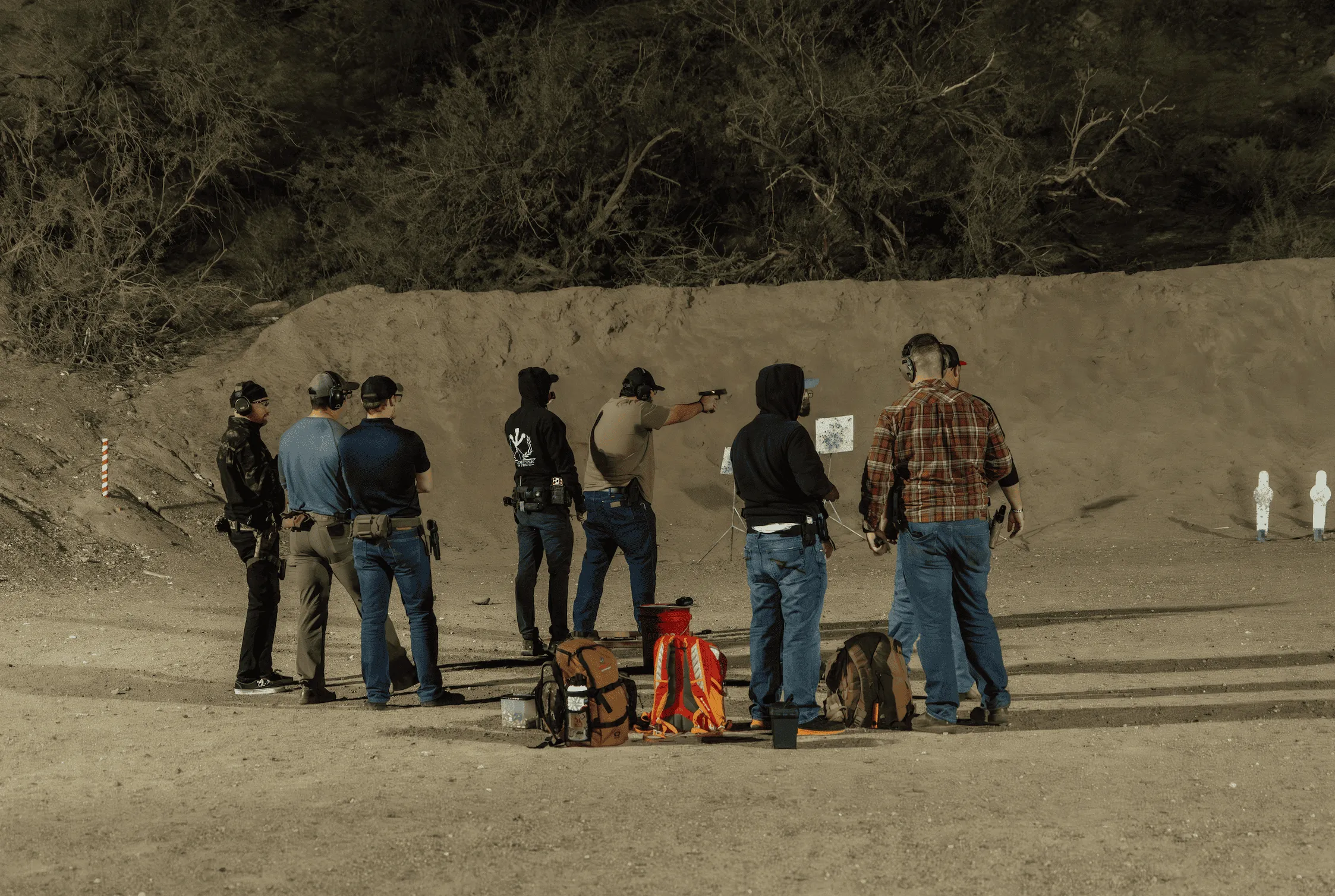 A line of shooters and an instructor engaging paper targets during a training evolution at an outdoor bay at Cowtown Range.