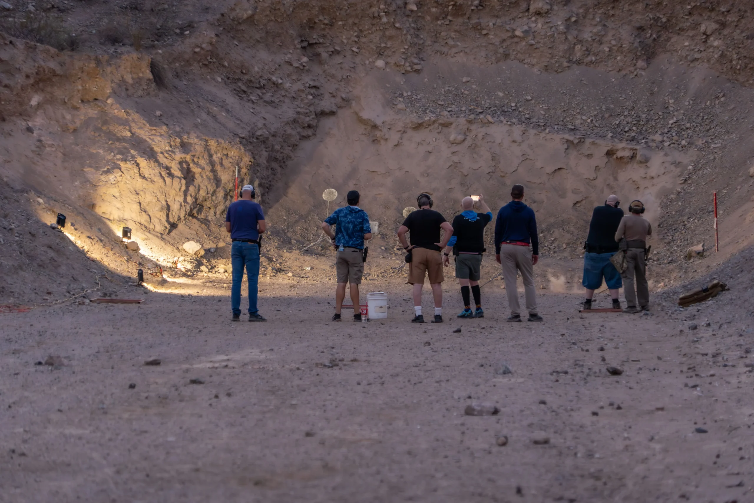 Shooters on the firing line engaging targets during low-light training on an outdoor bay at Cowtown Range.