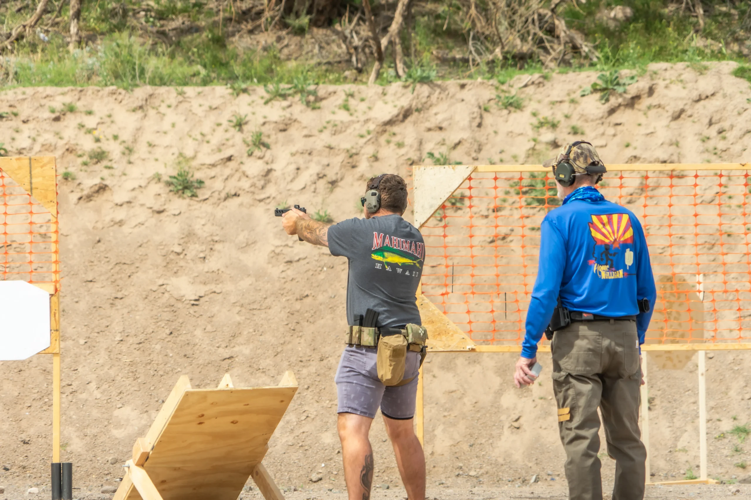 Instructor overseeing a shooter running a handgun through a dynamic movement drill on an outdoor bay.