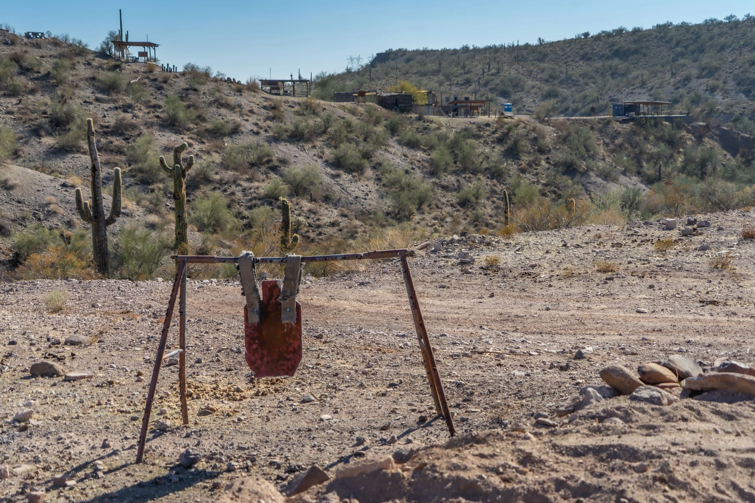 Impact-marked steel target on an outdoor bay with saguaro cacti and desert ridges in the background.