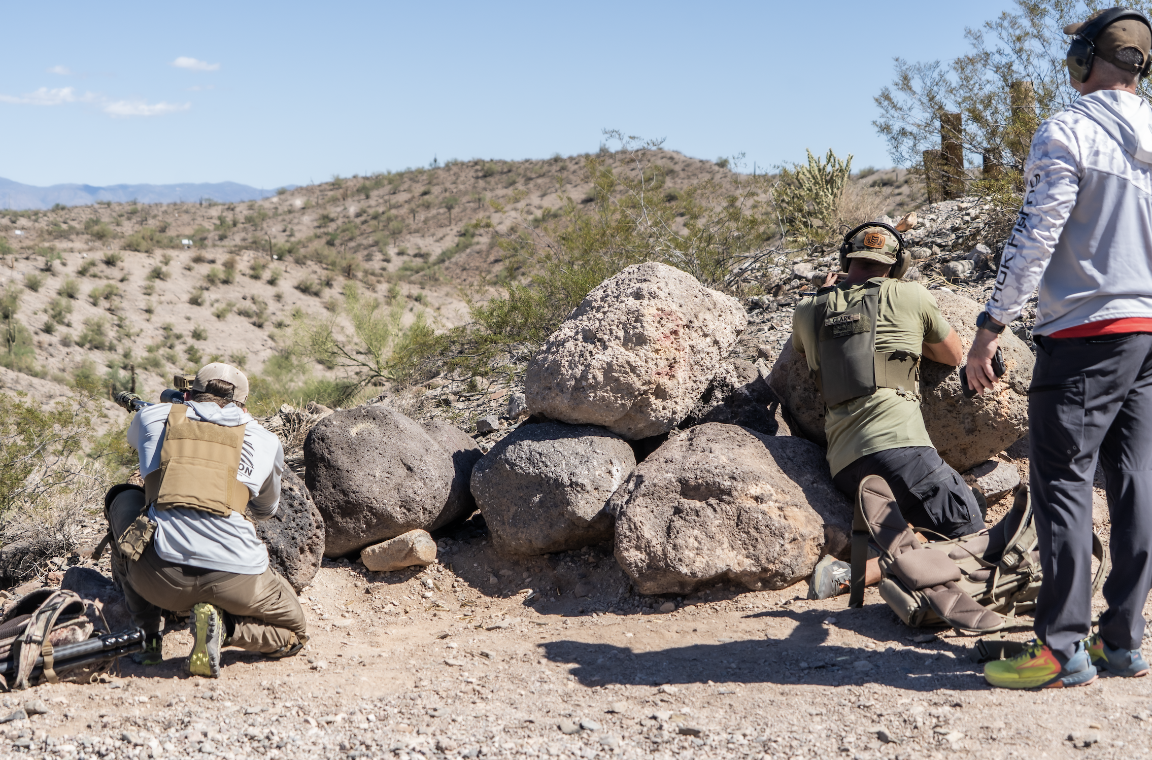Shooters utilizing natural rock cover for rifle training on an outdoor range.