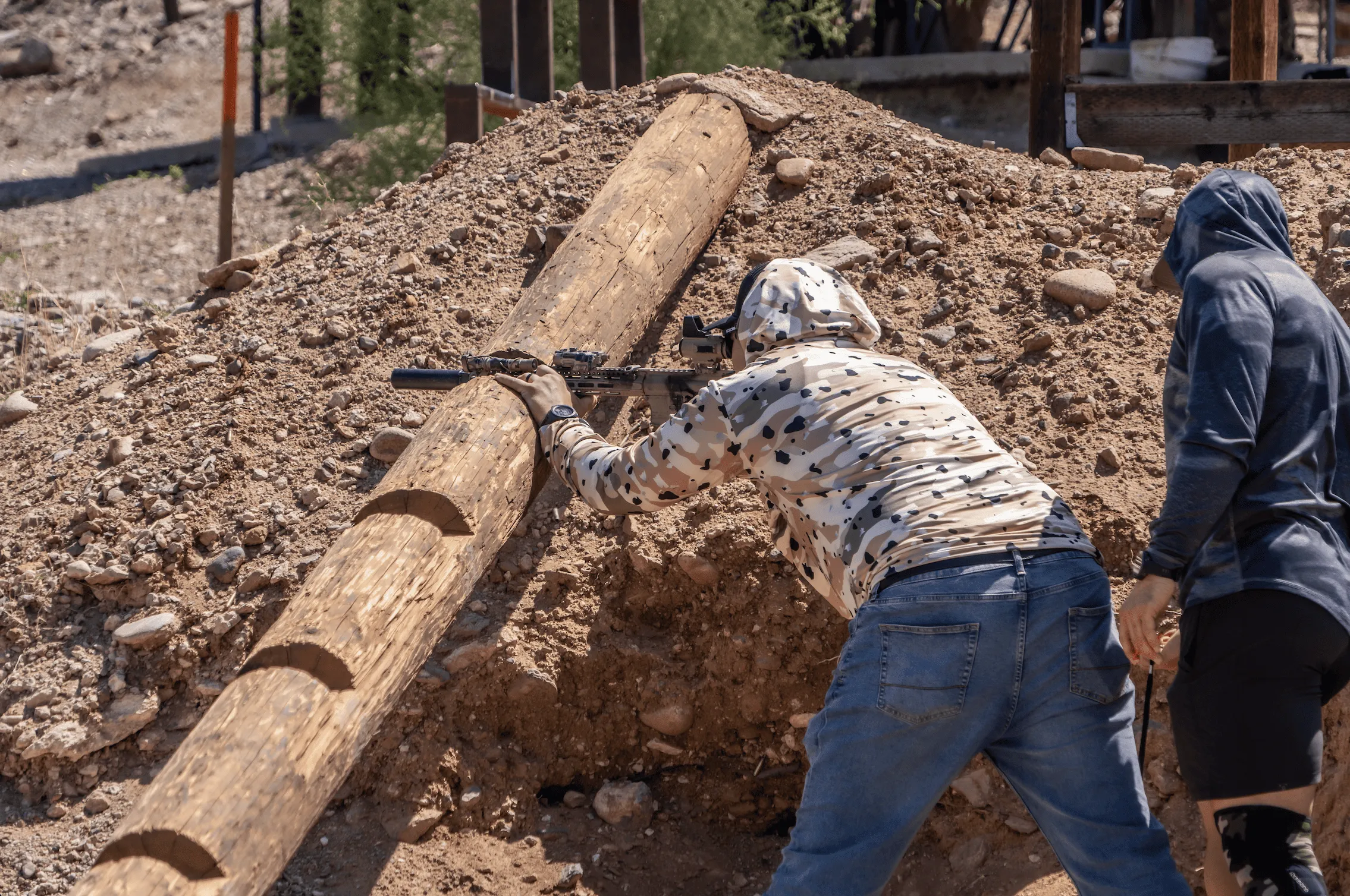 Shooter practicing positional rifle marksmanship behind a log prop on Cowtown Range's high-desert terrain.