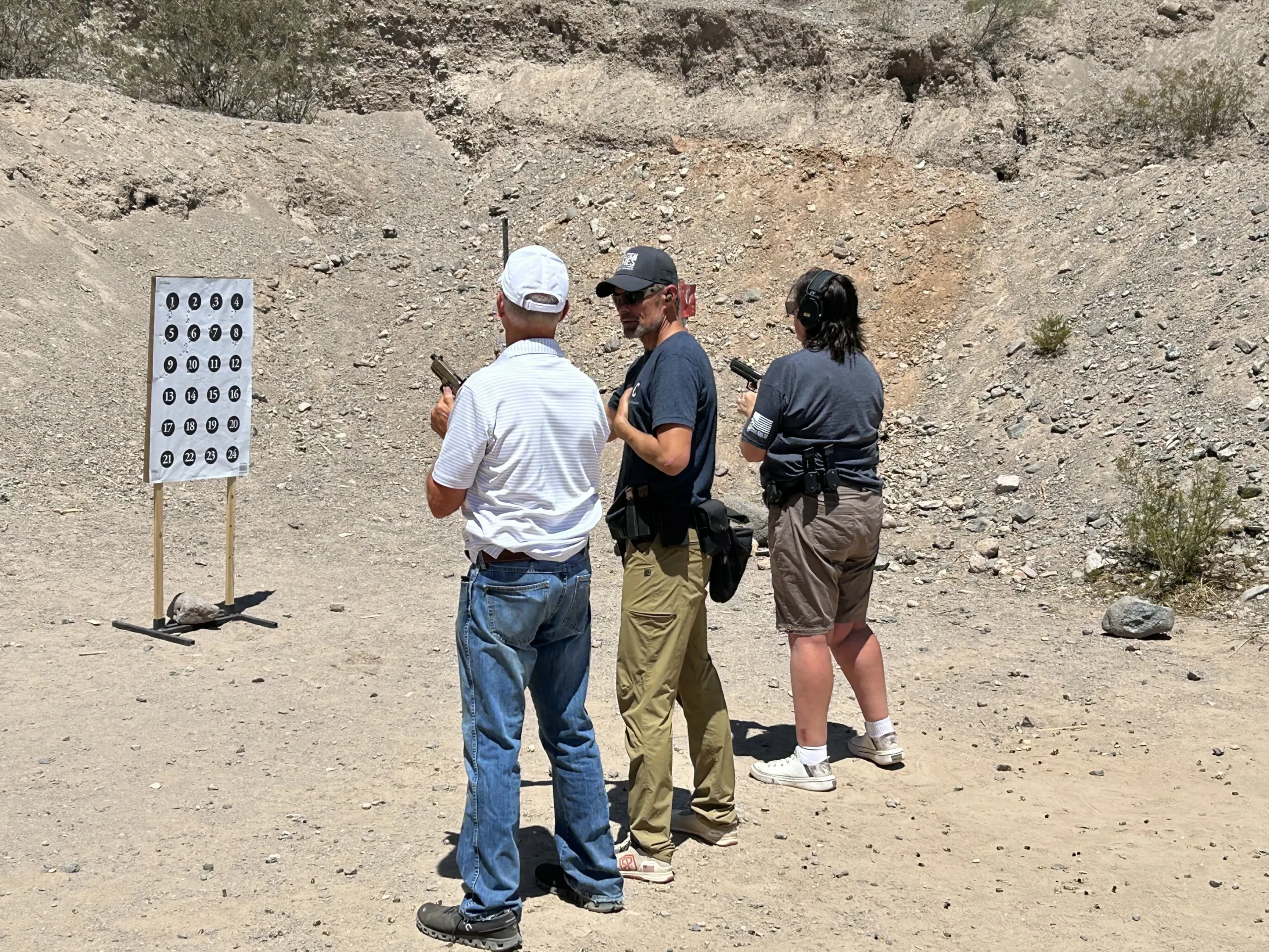 Shooters receiving personalized marksmanship coaching from instructors on a desert handgun bay.