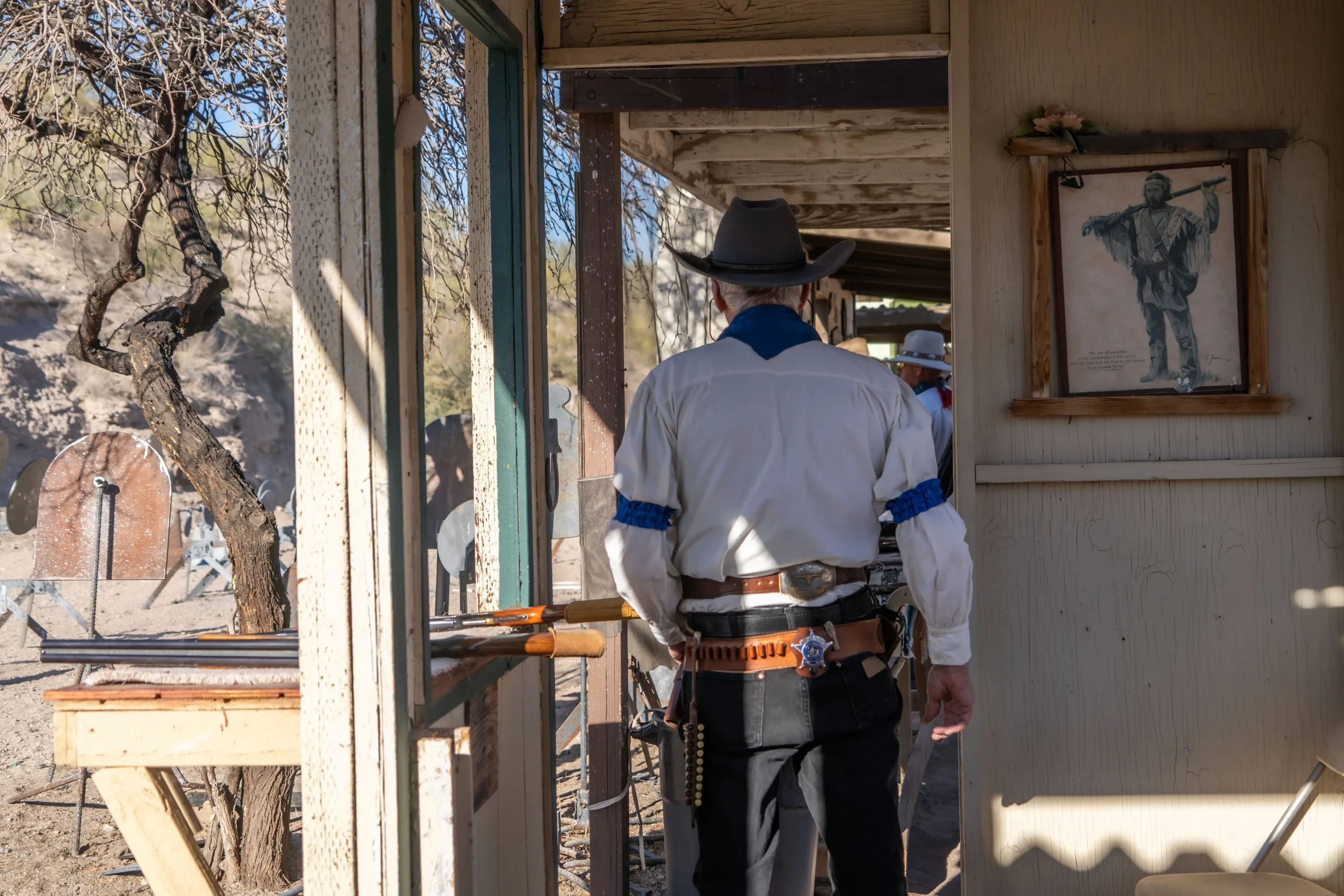 A Cowboy Action Shooting competitor wearing 19th-century attire stands at a range bay facing steel targets.