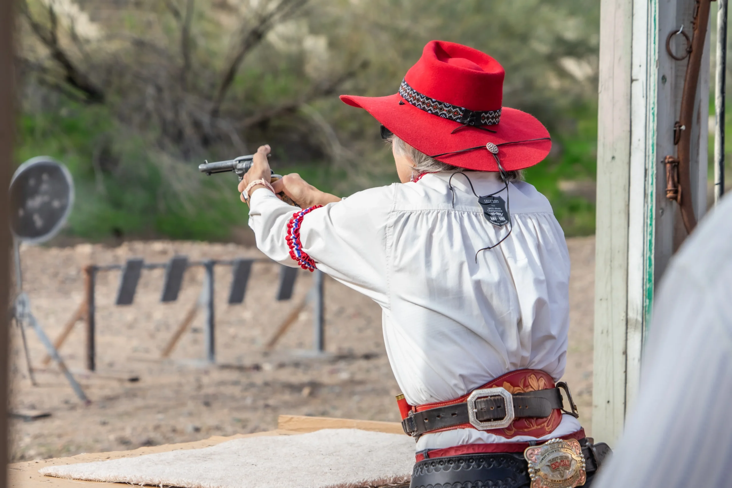 A competitor in a red hat fires a single-action revolver at steel targets during a SASS match.