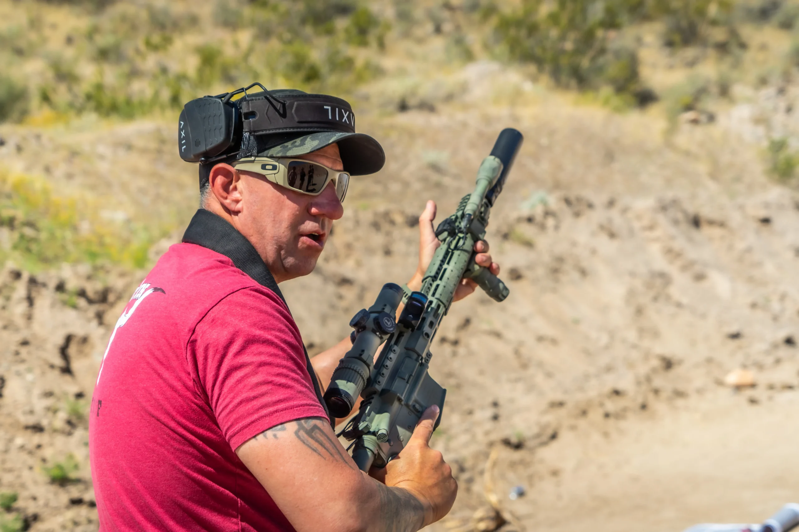 A shooter running a suppressed carbine platform with LPVO optics and earmuffs during a movement drill.