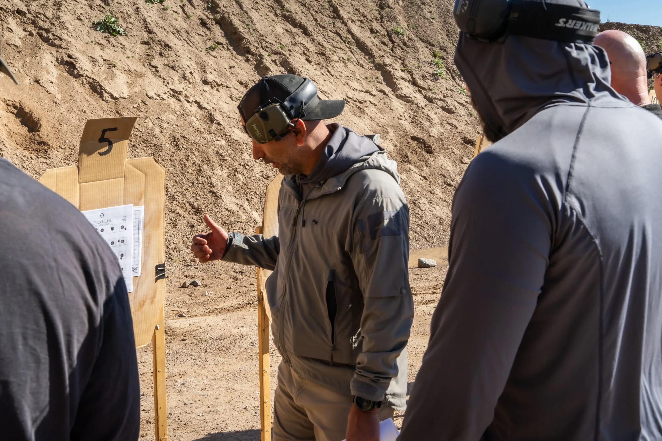 A Cowtown instructor conducting a target debrief with a squad of shooters reviewing dot drills downrange.