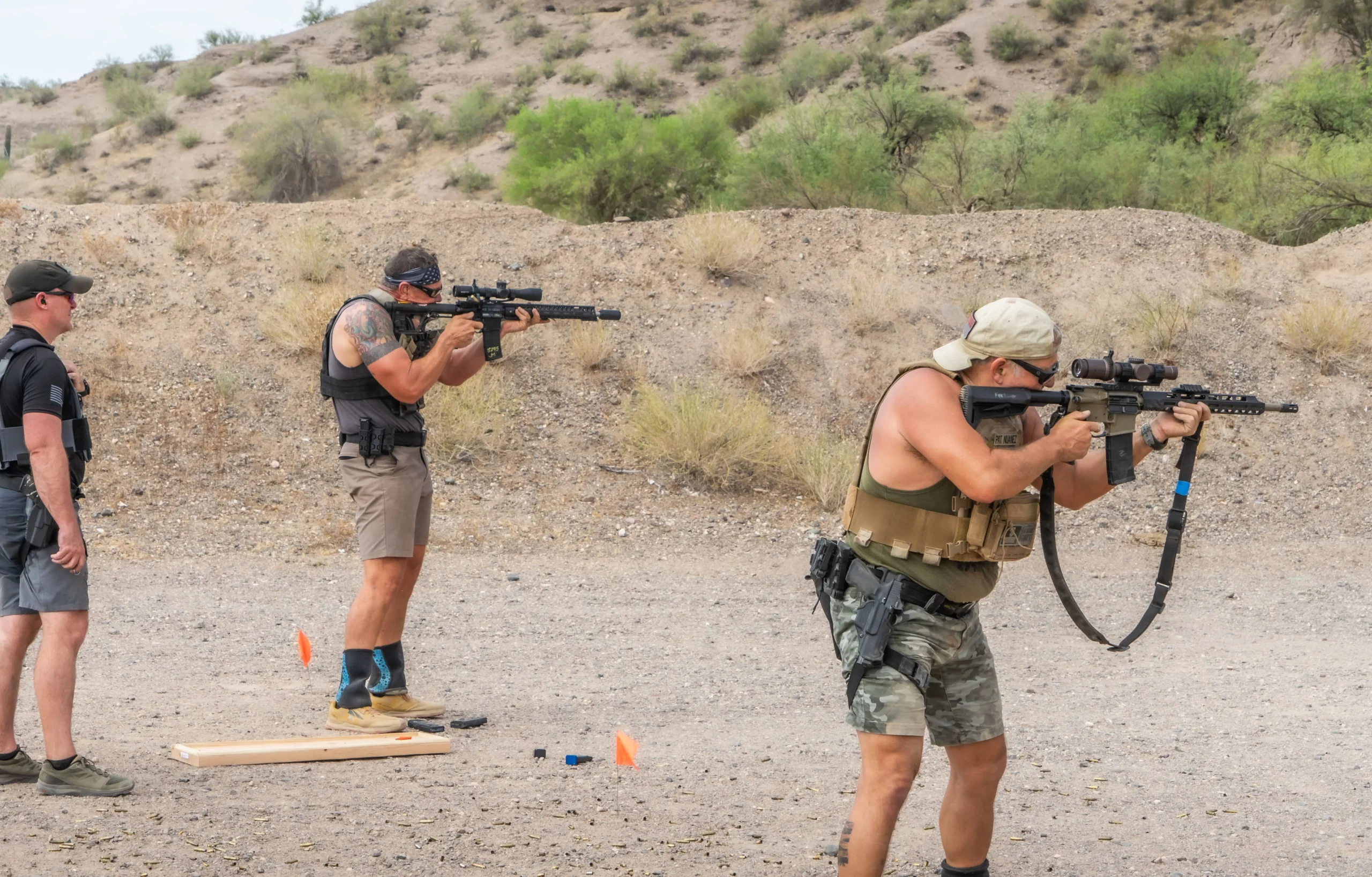 Shooters in chest rigs running carbine movement drills and controlling splits at an outdoor dirt bay.