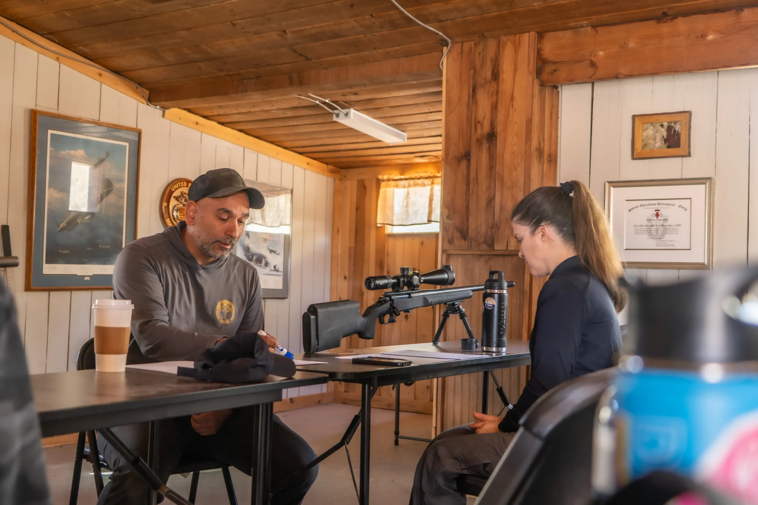 Instructor in a Cowtown shirt reviewing data with a student behind a precision rifle inside a range room.