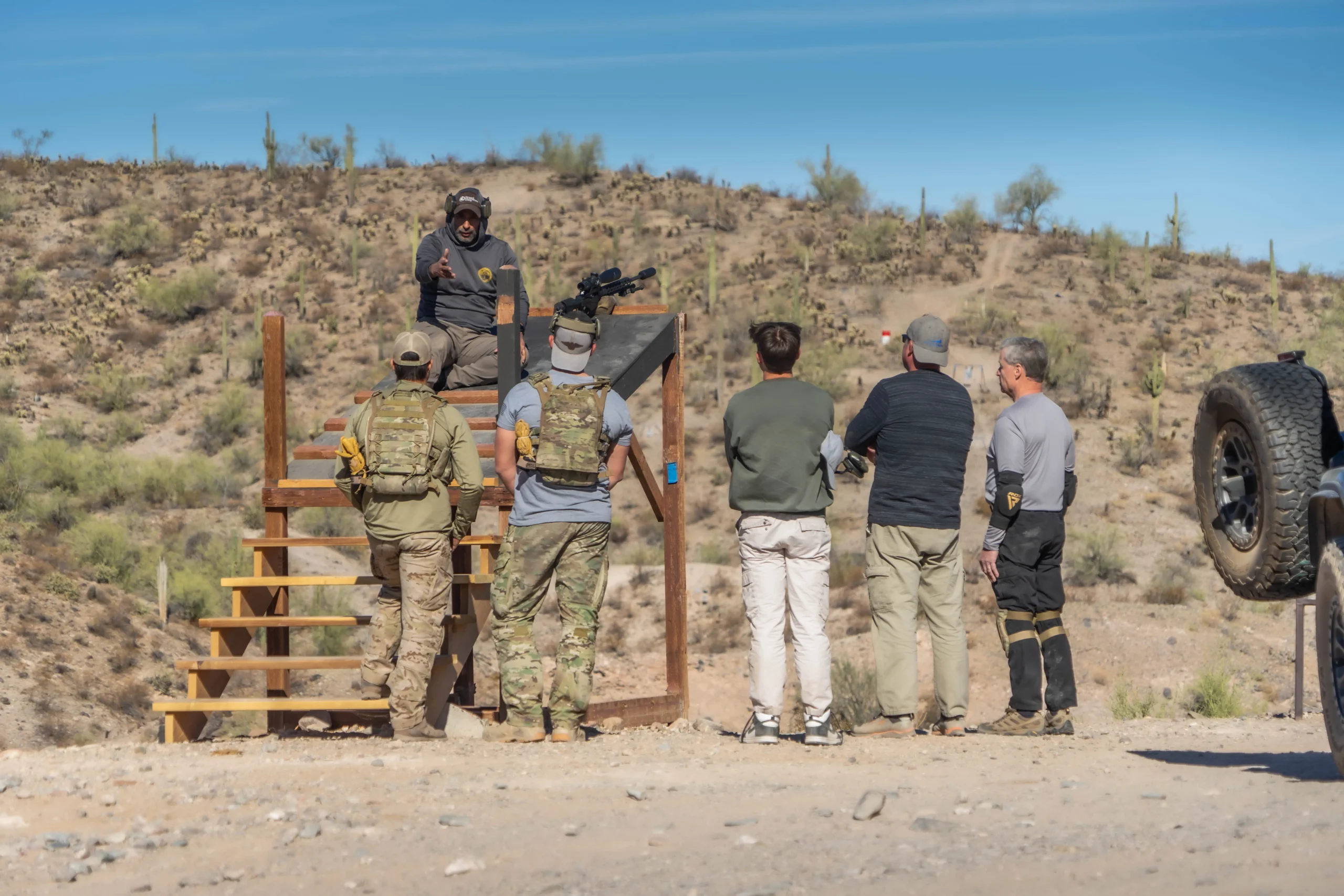Instructor providing platform briefing on a staircase barrier to serious shooters during an outdoor course.