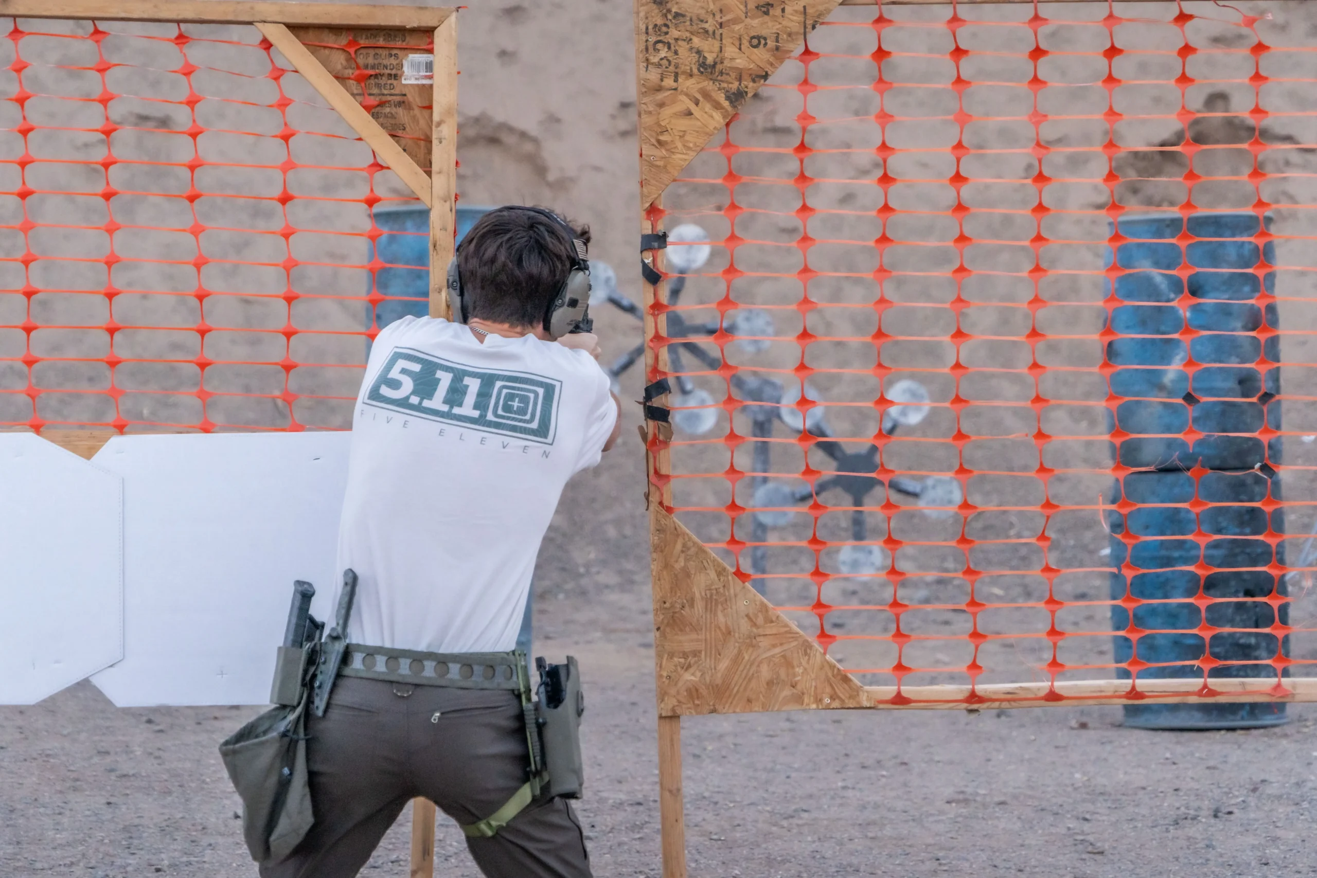 A competitor running pistol drills through a barricade stage toward a Texas star steel target downrange.