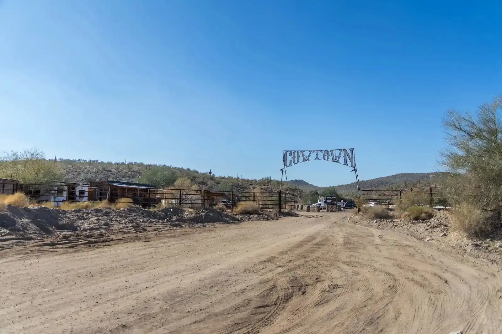 Wide shot of the dirt entrance road leading under the iconic steel Western Cowtown sign in the desert.